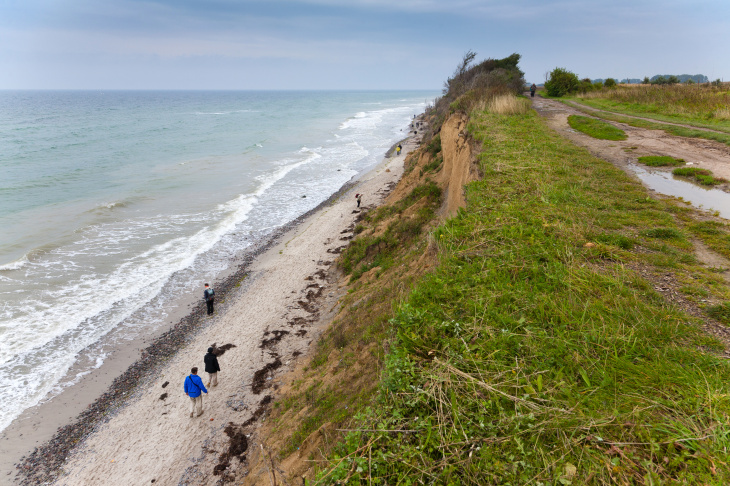Land fällt in das Meer ab. Unten sind Spaziergänger